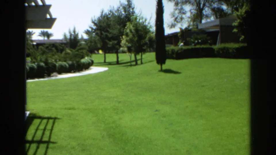 1968 Scottsdale outdoor view transitioning to a manicured green lawn with trees, shrubs, a curving path, and building edges.