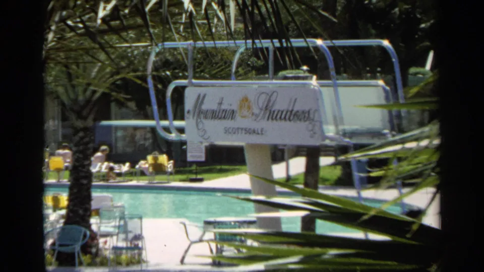 1968 Scottsdale resort pool view with the Mountain Shadows sign, turquoise water, lounge chairs, and palm landscaping.