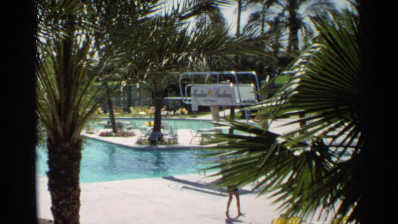 1968 Scottsdale resort pool scene framed by palm trees, with a turquoise pool, diving board, and Mountain Shadows sign visible.