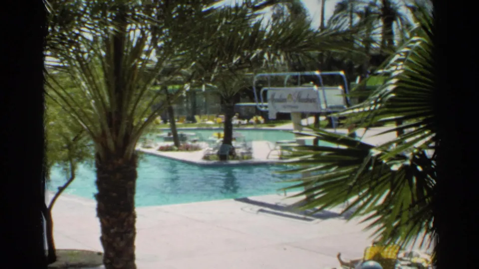 Scottsdale resort pool viewed through palm fronds, showing the diving board, deck, and Mountain Shadows sign in bright sun.