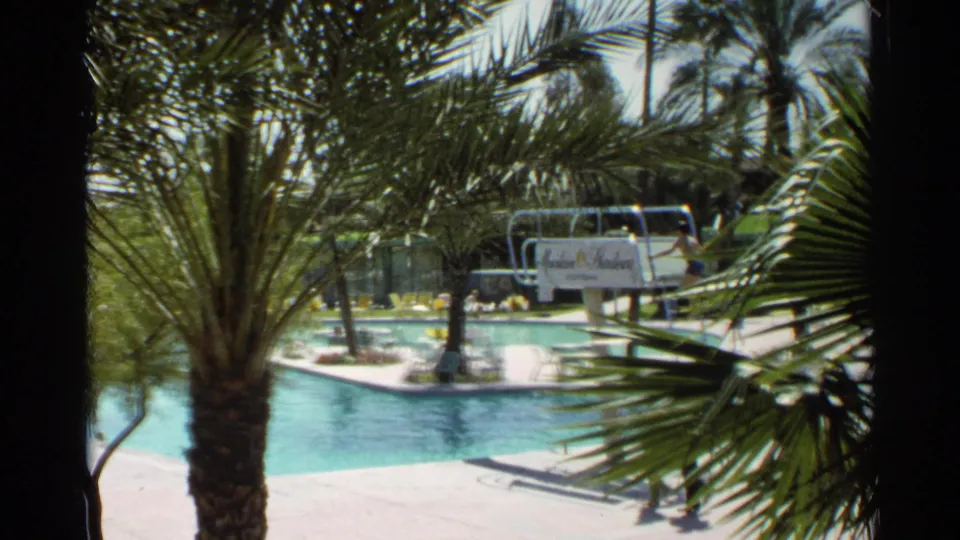 Scottsdale resort pool scene with palms, a diving board, Mountain Shadows sign, and small figures moving near the pool deck.