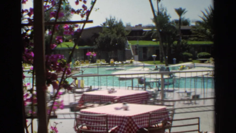 1968 Scottsdale resort terrace with red-and-white checkered tables, patio railings, flowering vines, swimmers, and lounge chairs near the pool.
