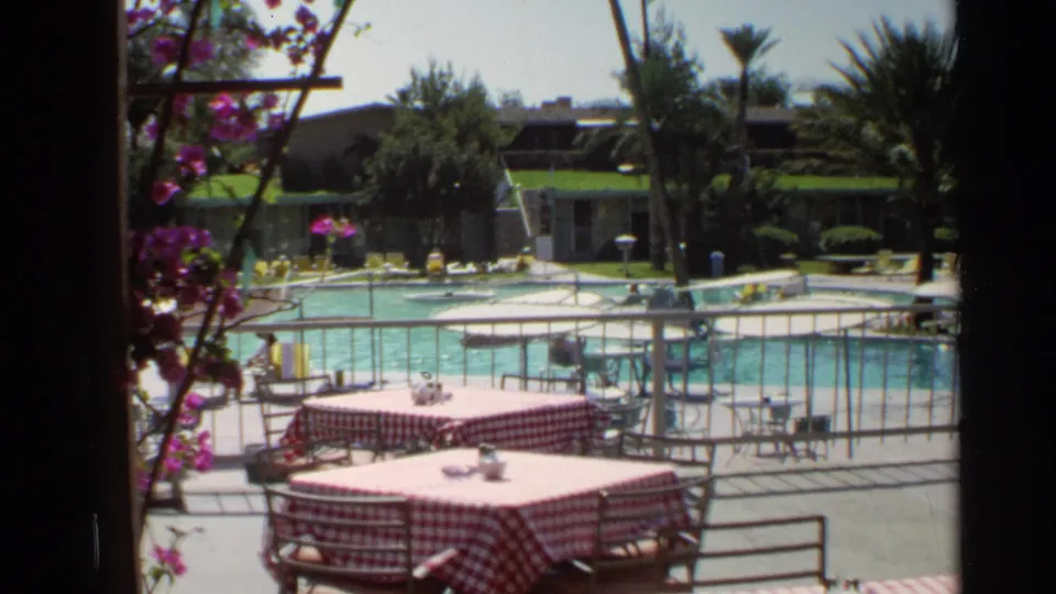 1968 Scottsdale resort view from an outdoor dining terrace toward the pool, lounge chairs, landscaped shrubs, and low resort buildings.