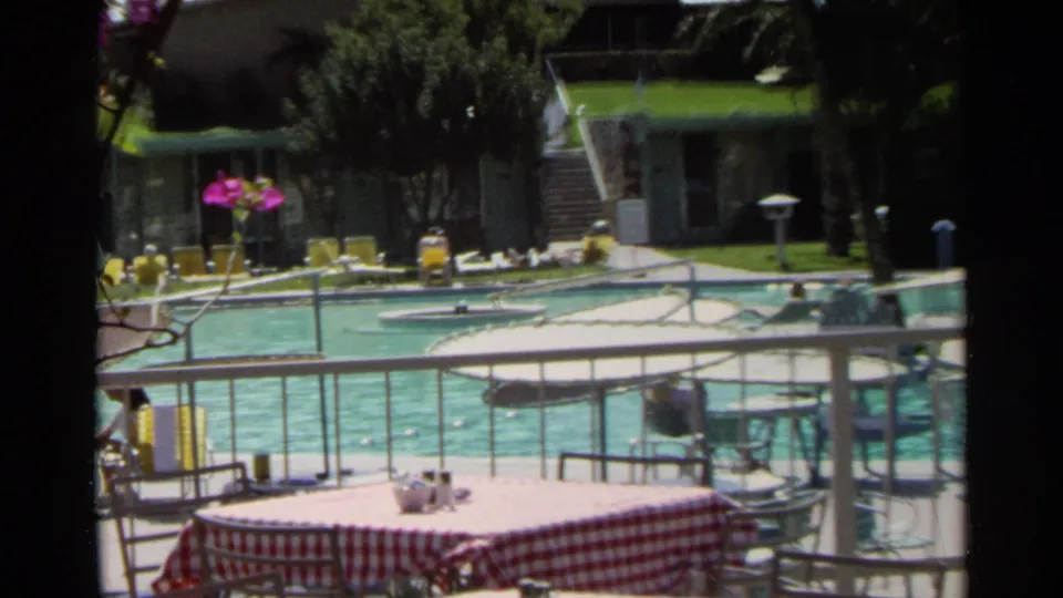 Scottsdale pool scene with a foreground checkered table, turquoise water, yellow lounge chairs, flowers, and low poolside buildings.