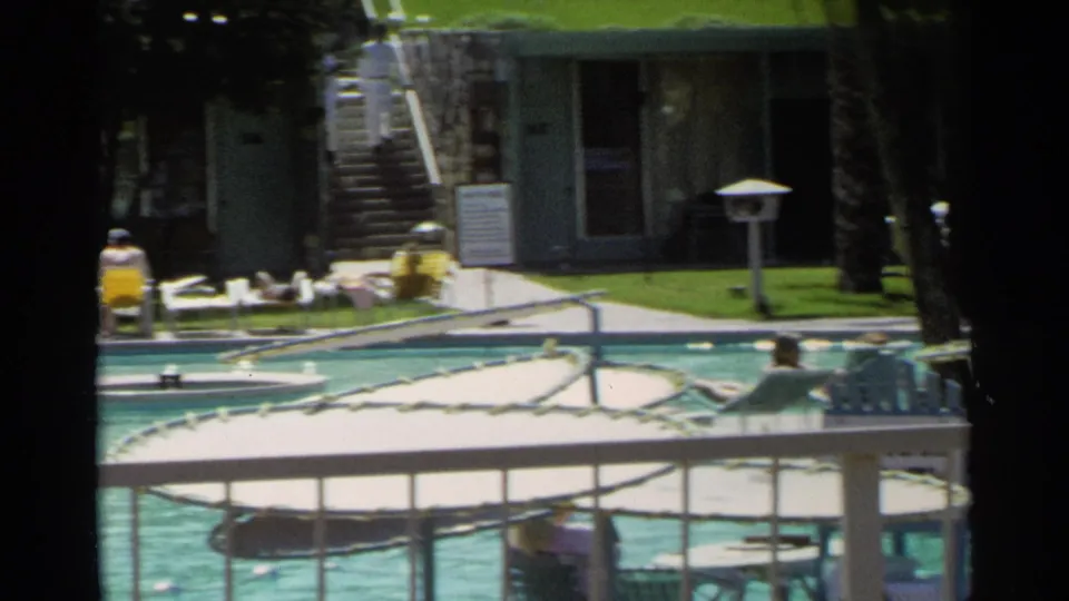 1968 Scottsdale pool area with turquoise water, metal railings, lounge chairs, palm trunks, and low resort-style buildings.