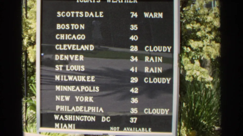 1968 Scottsdale 8mm still showing a framed weather board with U.S. city temperatures and condition labels outdoors.
