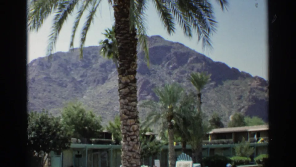 1968 Scottsdale vacation frame with palm trees, landscaped grounds, a low structure, and a rugged mountain backdrop.
