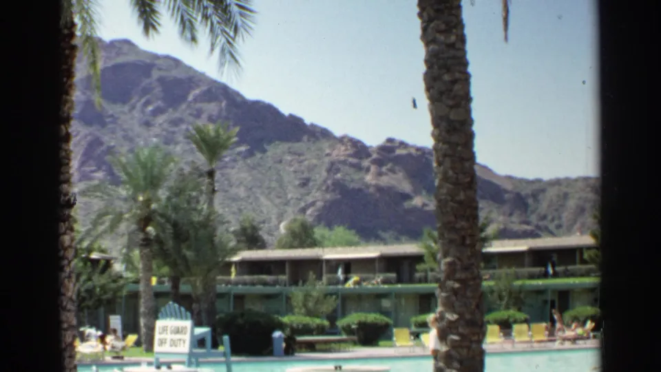 1968 Scottsdale resort footage showing a pool deck with palms, yellow chairs, guests, motel rooms, and desert mountains in the background.