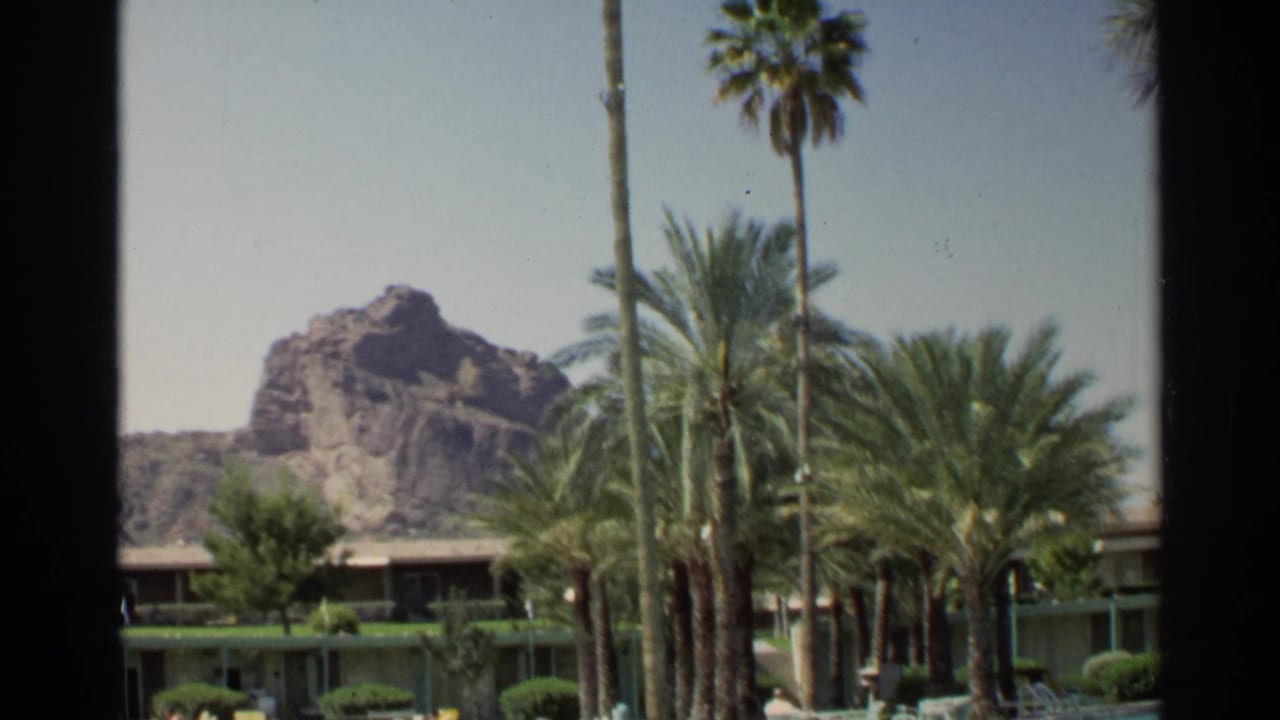 1968 Scottsdale resort view with palms, a low hotel building, and a rocky desert backdrop seen across the pool area.