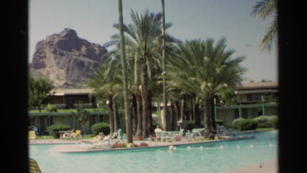 Scottsdale resort pool scene from 1968 with palms, lounge furniture, hotel rooms, and a rocky desert formation behind them.