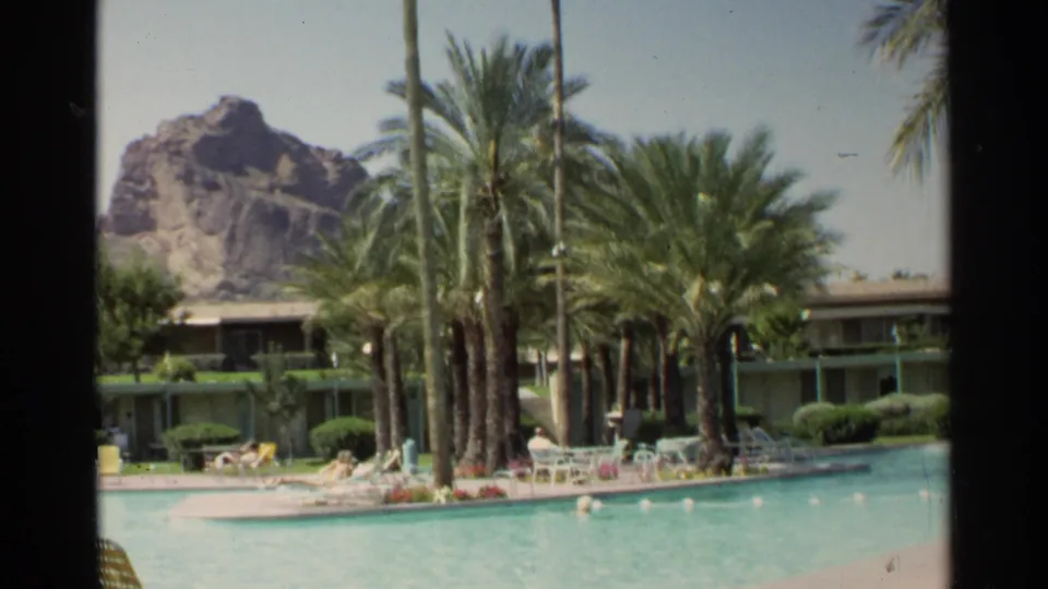 Scottsdale resort pool scene from 1968 with palms, lounge furniture, hotel rooms, and a rocky desert formation behind them.