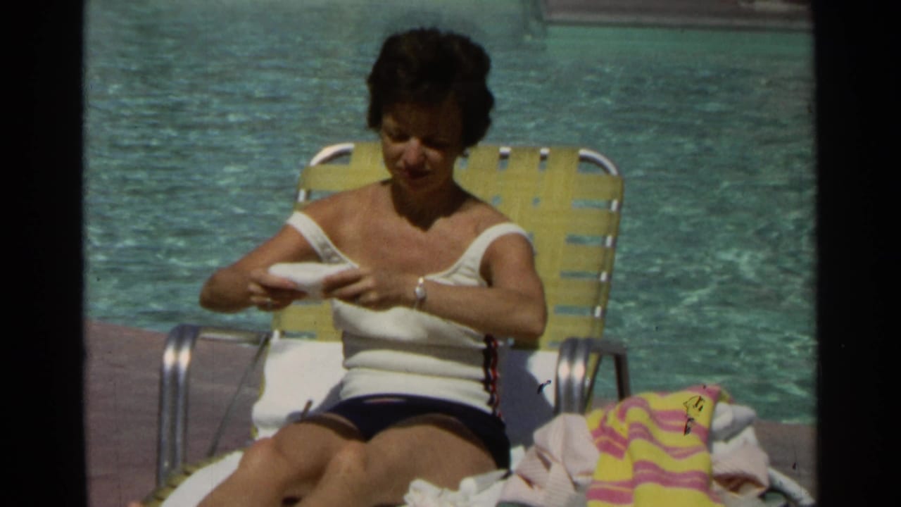 Woman seated on a yellow lounge chair beside a swimming pool applying lotion to her arm.