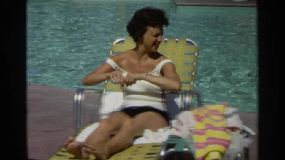 The poolside scene shows the woman seated on a yellow lounge chair, with bright water and a striped towel beside her.