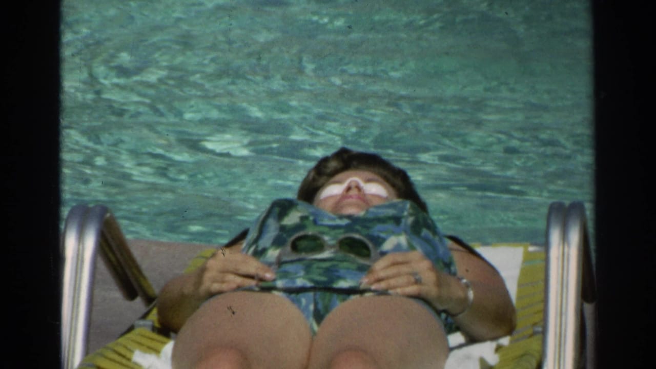 Woman reclines on a lounge chair beside a swimming pool with an eye mask on her face.
