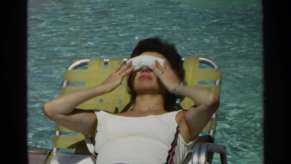 In supplied 1968 Scottsdale footage, a woman sunbathes on a yellow lounge chair with a white eye mask beside the pool.