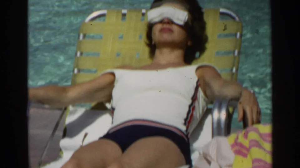 A woman in a white swimsuit rests on a yellow poolside lounge chair in the Scottsdale 1968 home-movie scene.