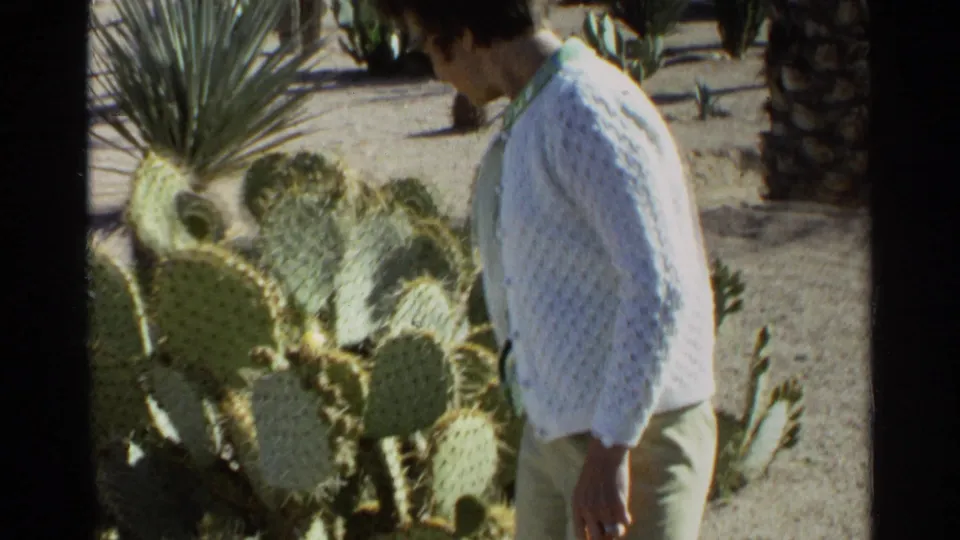 The woman looks down while walking past cactus pads and desert plants in Scottsdale, Arizona, according to the clip metadata.