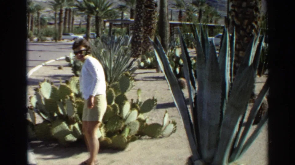 A wider 1968 Scottsdale frame shows the woman beside prickly pear cactus, a large agave, palm trunks, and parked cars in the background.