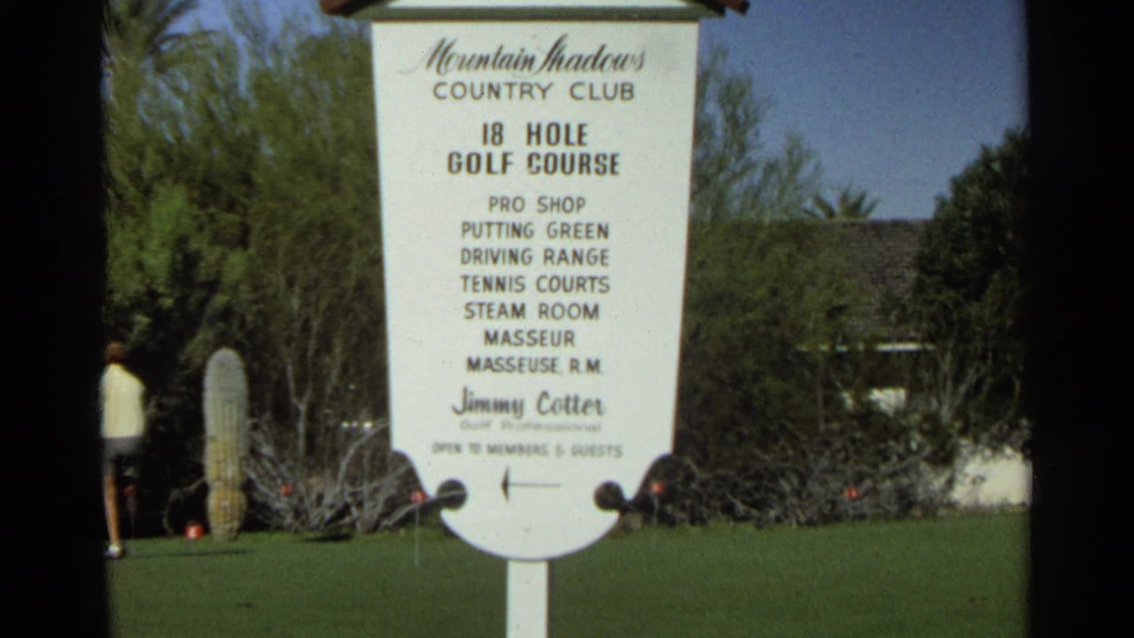 Mountain Shadows Country Club sign on a green lawn with desert plants behind it.