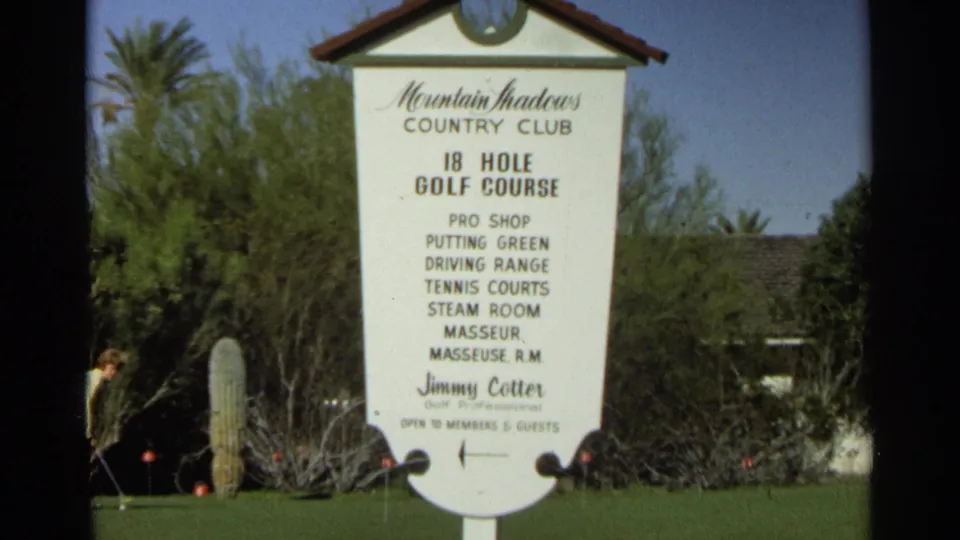 Scottsdale, Arizona frame showing the Mountain Shadows Country Club sign, golf amenities text, cactus, desert shrubs, and a golfer near the left side.