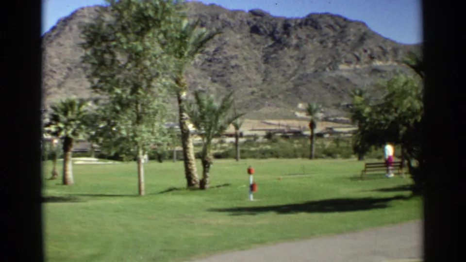 A wider 1968 Scottsdale view shows the landscaped golf course, palm trees, desert mountains, paved path, course marker, and a distant person near the right edge.