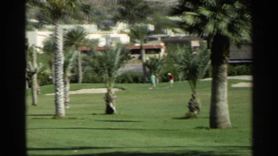 1968 Scottsdale golf course view with palms, cacti, green fairway, distant golfers, low buildings, and mountain terrain.