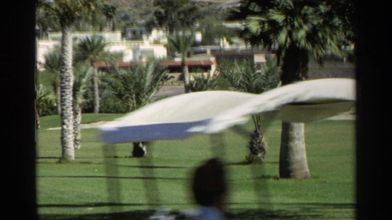 Motion-blurred golf cart crossing a 1968 Scottsdale fairway with palms, cacti, and distant course landscaping.