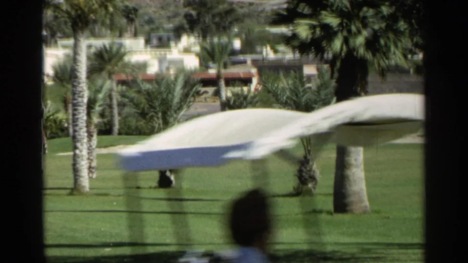 Motion-blurred golf cart crossing a 1968 Scottsdale fairway with palms, cacti, and distant course landscaping.