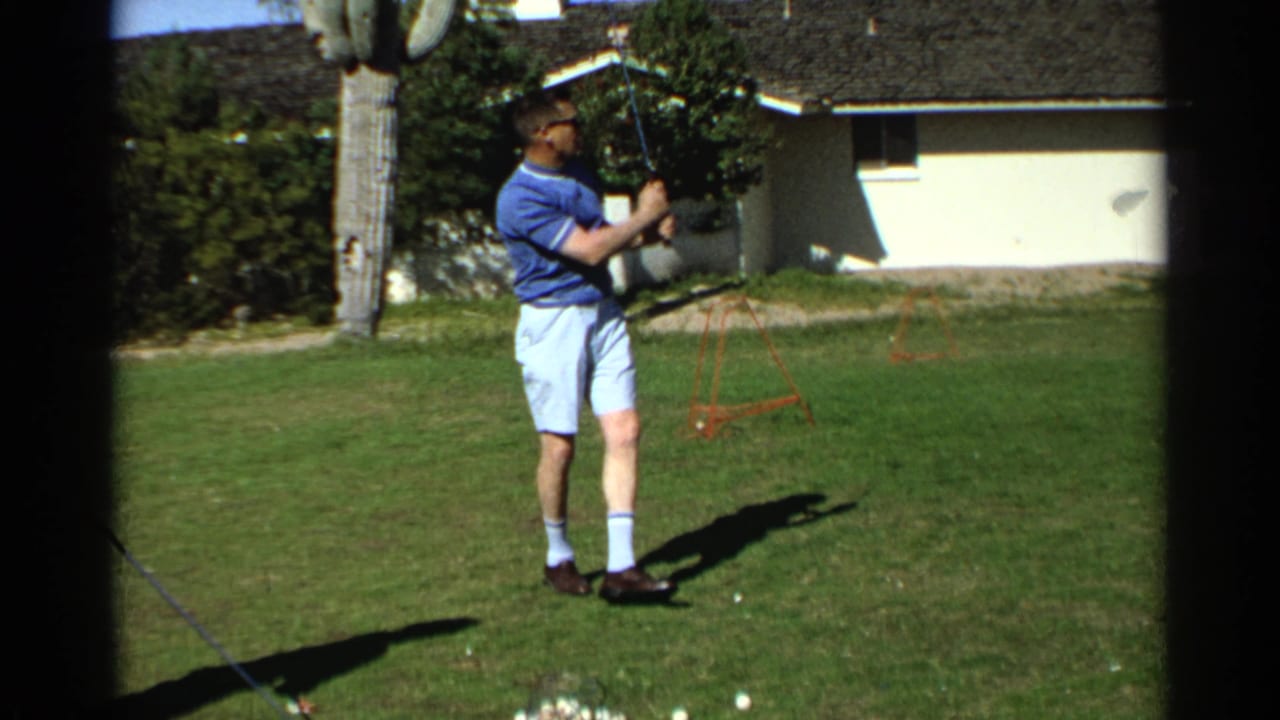 In the Scottsdale backyard scene, the man pauses after a golf swing with the lawn, house, and saguaro visible behind him.