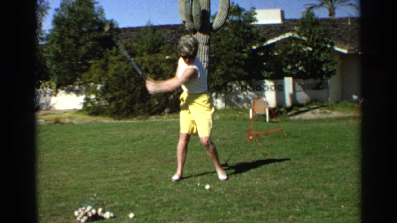 Woman in yellow shorts preparing to swing a golf club on a backyard lawn.