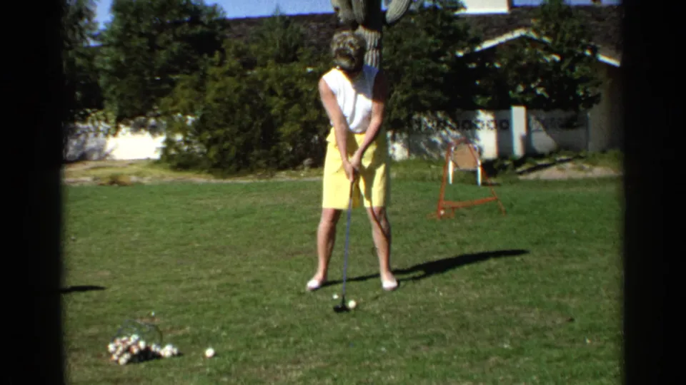 In 1968 Scottsdale home-movie footage, a woman in a white sleeveless top and yellow shorts prepares to swing a golf club on a backyard lawn.