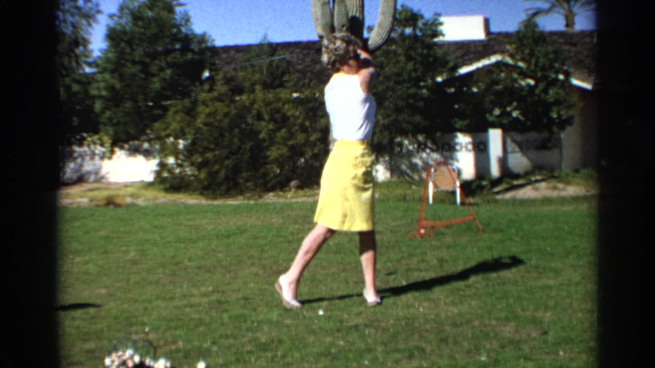 Woman in a yellow skirt follows through on a golf swing on a sunny lawn.