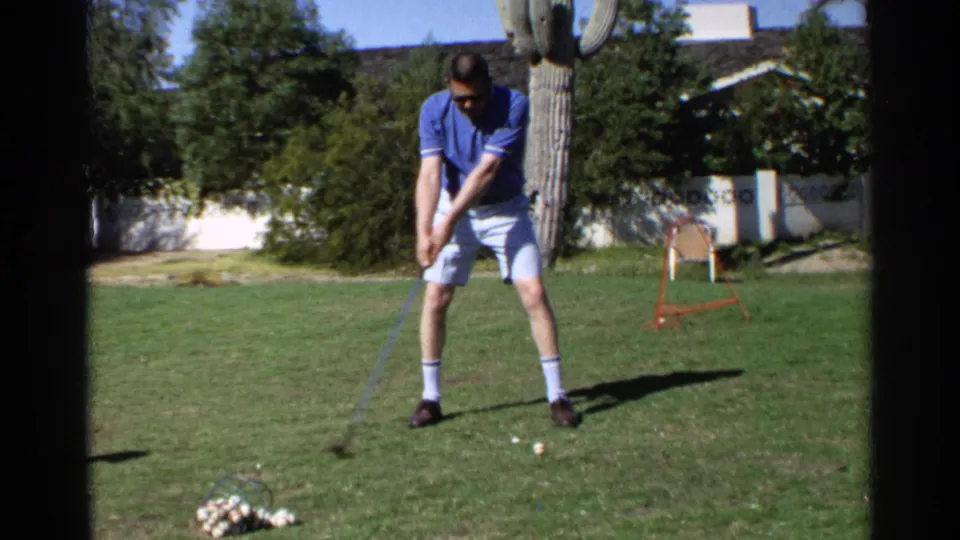 In 1968 Scottsdale backyard footage, a man in a blue polo and white shorts prepares to swing a golf club on a lawn.