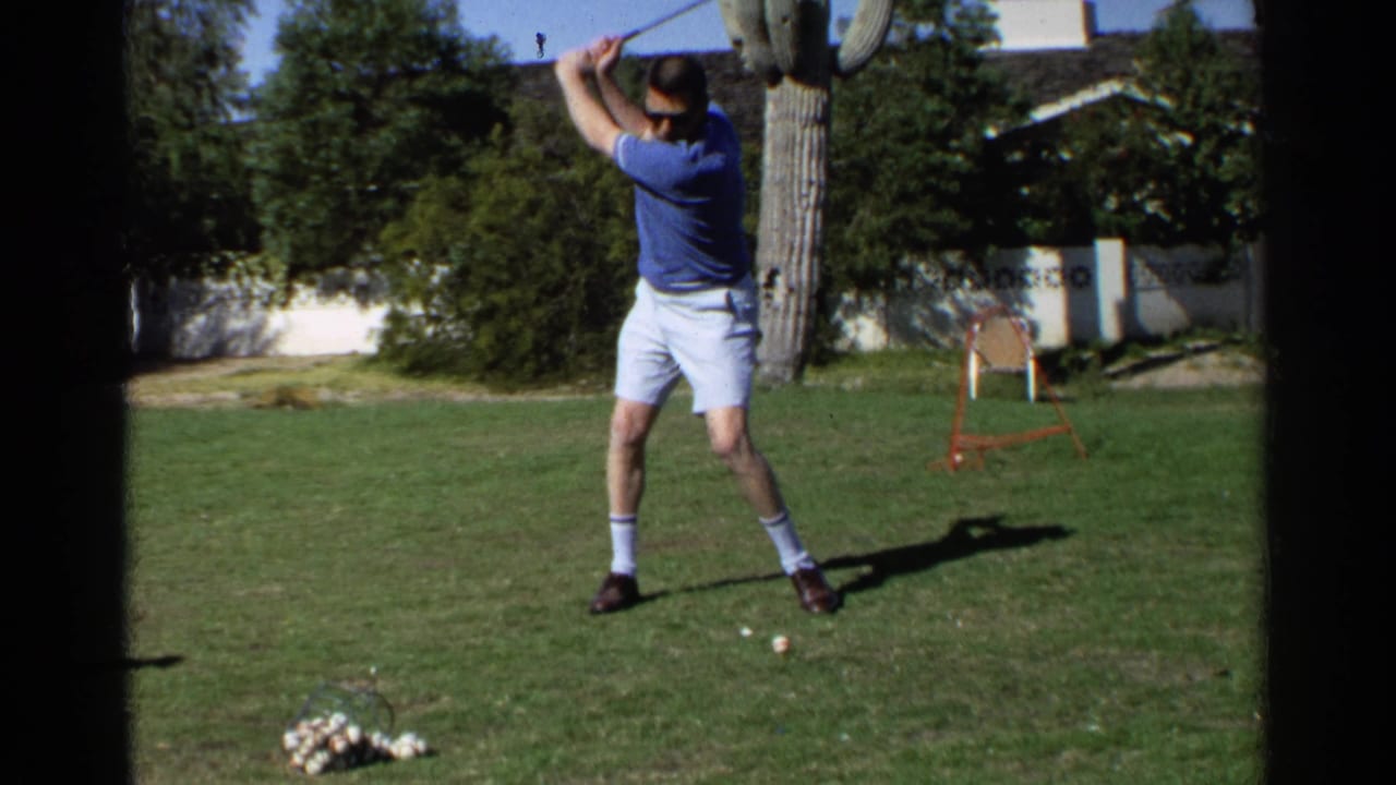 Man lifts a golf club into a backswing on a sunny lawn.