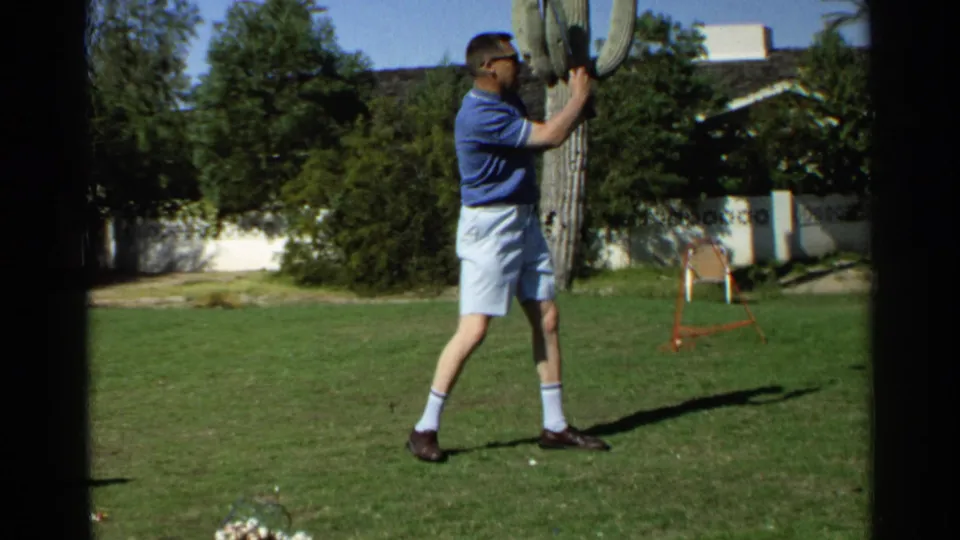 The man finishes his backyard golf motion in Scottsdale, with the cactus, lawn, chair, and residential exterior still visible.