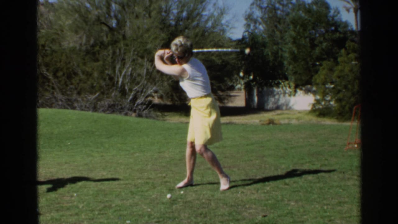 Woman in a yellow skirt begins a golf swing on a grassy course.