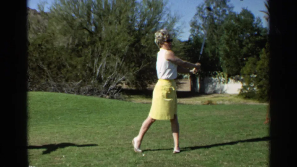 The woman golfer stands in profile at the end of her swing in Scottsdale, Arizona, with 8mm grain and bright outdoor color.