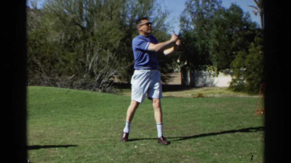 The golfer follows through during a swing in 1968 Scottsdale home-movie footage, with trees and open grass in the background.