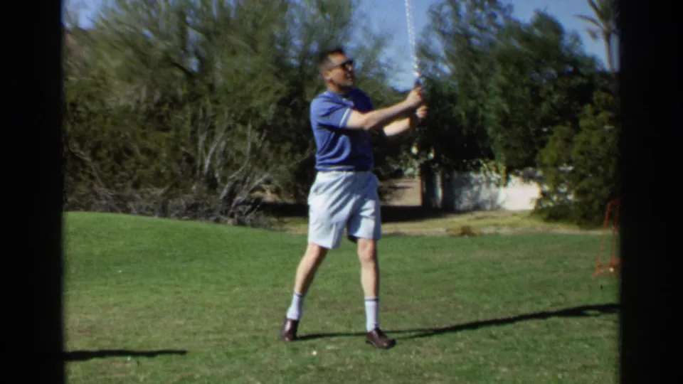 The 1968 Scottsdale 8mm frame shows the golfer on a green lawn, partly bordered by dark film gate edges and desert vegetation.