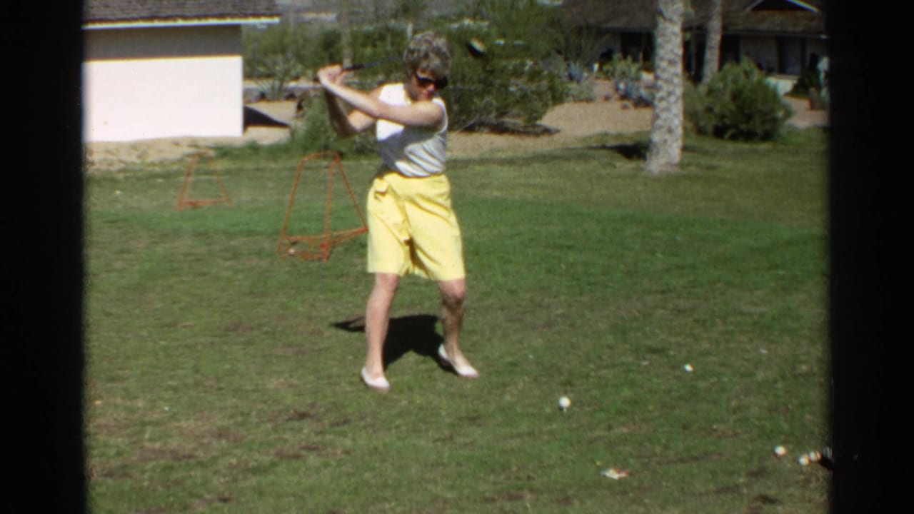Woman in sunglasses preparing to swing a golf club on a lawn.