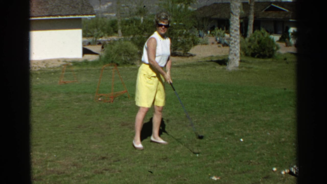 Woman in sunglasses stands on grass with a golf club near golf balls.