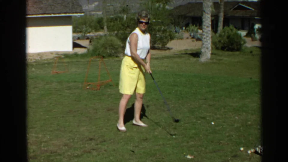 In Scottsdale, Arizona, 1968, a woman in a white sleeveless top and yellow skirt prepares with a golf club on a grassy yard.