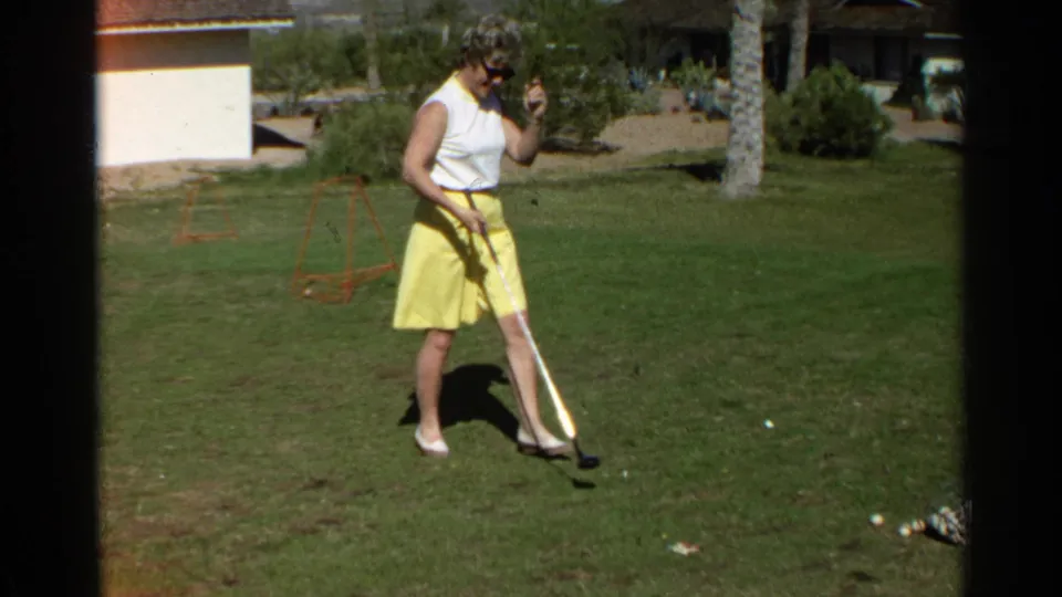 A woman in yellow skirt and sunglasses walks toward the golf balls with her club in the Scottsdale, Arizona footage.