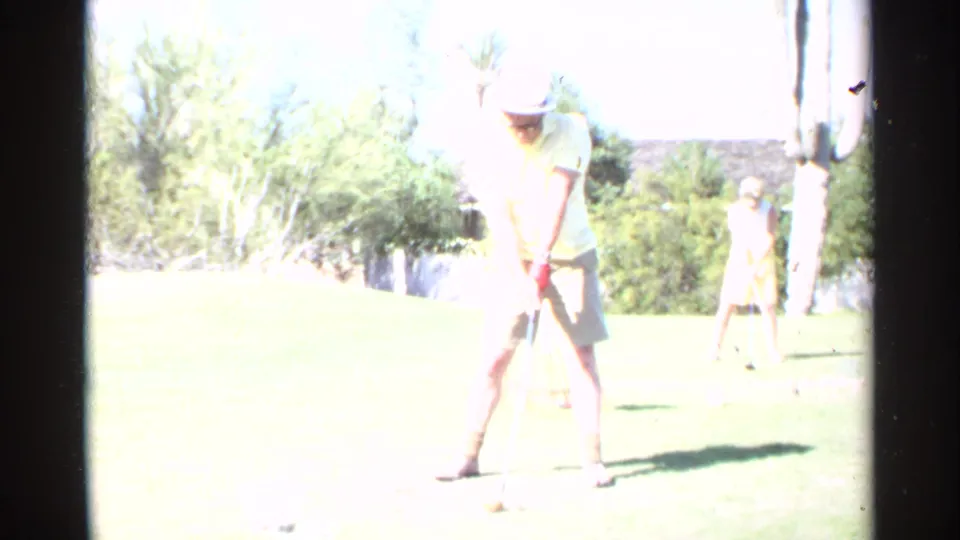 Brightly overexposed 8mm frame shows a man with a golf club on a sunny Scottsdale lawn, with another person in yellow nearby.