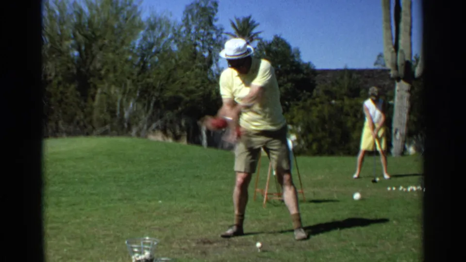 A 1968 Scottsdale home-movie frame shows a man mid-swing on grass, with a woman, golf balls, trees, and a tall cactus behind him.