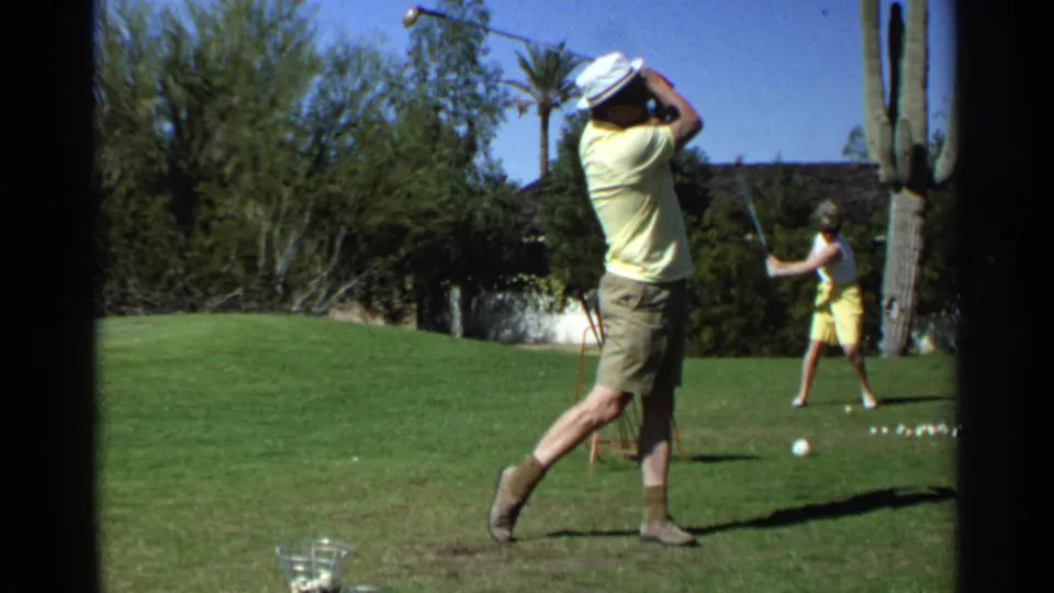 A Scottsdale desert golf range scene shows a man completing his swing while a woman practices near golf balls and cactus.