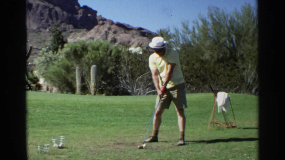 A man prepares to hit a golf ball on a Scottsdale range, framed by saguaro cactus, desert trees, and rocky hills.