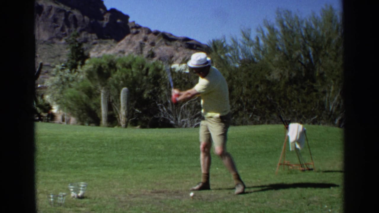 Man in a yellow shirt begins a golf swing on a green desert course.