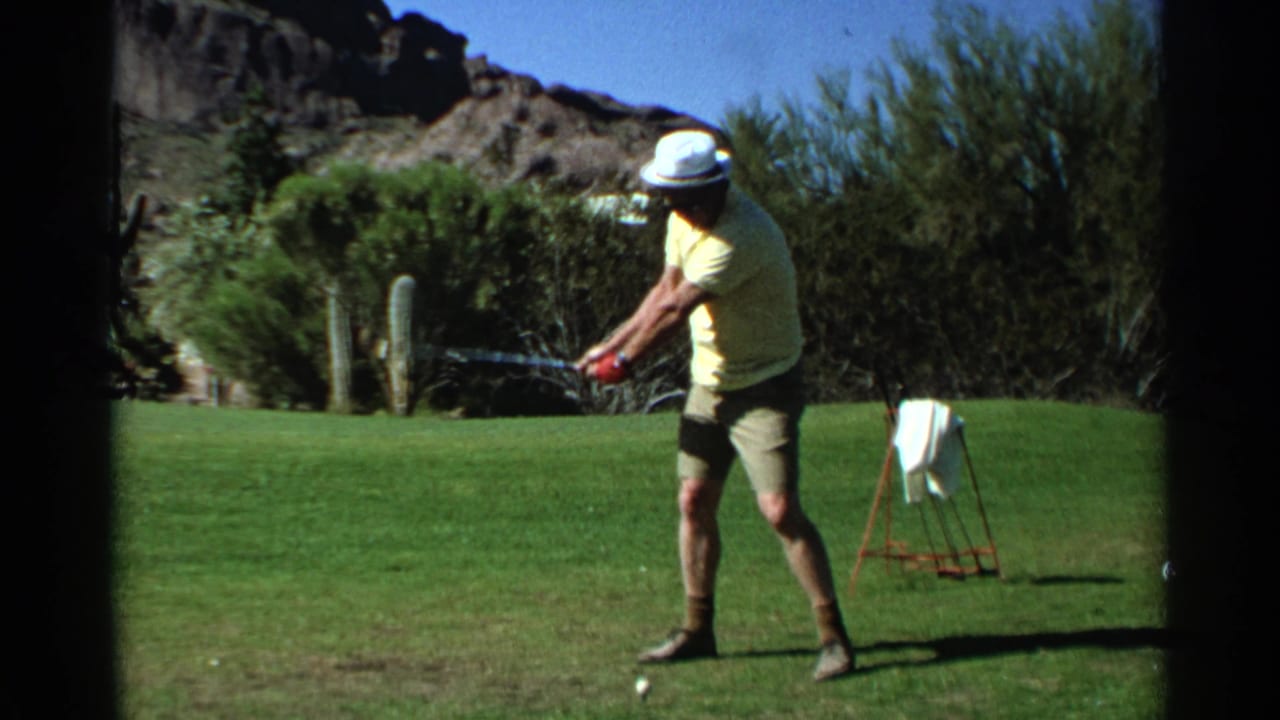 Man in a yellow shirt addresses a golf ball on a desert golf course.
