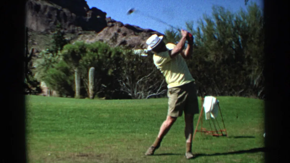 A man in 1968 Scottsdale follows through on a golf shot, leaning back as the club rises above him on the desert course.